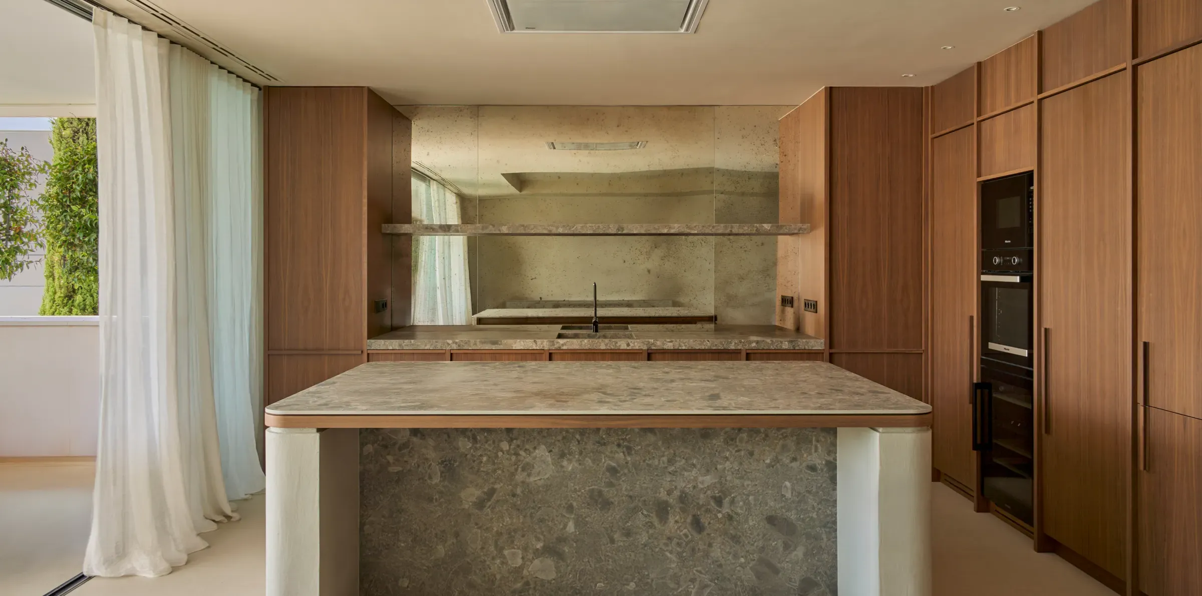 Refined kitchen interior with stone island, minimalist stools, and mirrored backsplash in Ibiza residence
