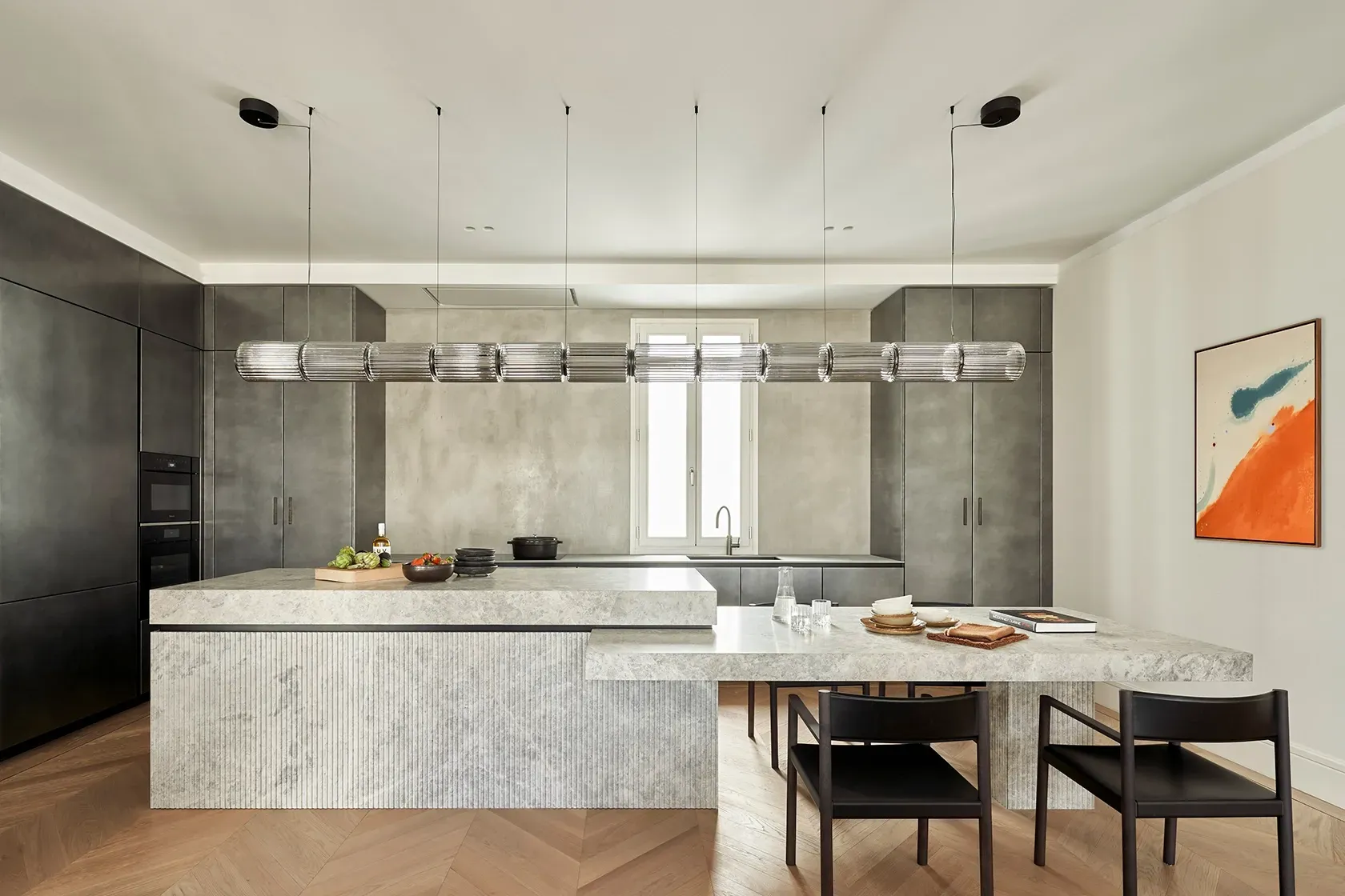 Modern kitchen with dark cabinetry, sculpted stone island, vertical lighting feature, and bold abstract artwork on a clean white wall.