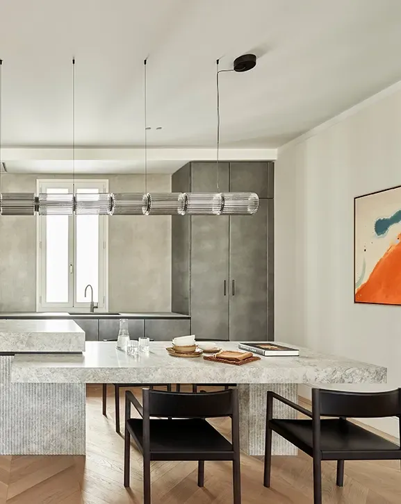 Modern kitchen with dark cabinetry, sculpted stone island, vertical lighting feature, and bold abstract artwork on a clean white wall.