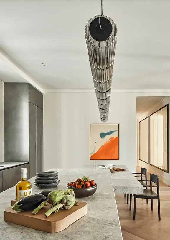 Open kitchen space with textured grey island, organic still life arrangement, and connection to a bright living area with neutral-toned furniture.