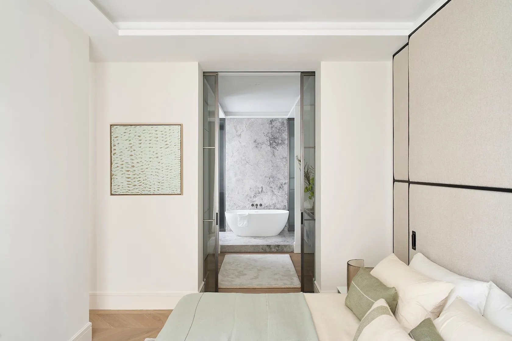 Master bedroom with upholstered wall paneling and neutral tones, leading to a marble-finished ensuite bathroom with freestanding tub and soft lighting.
