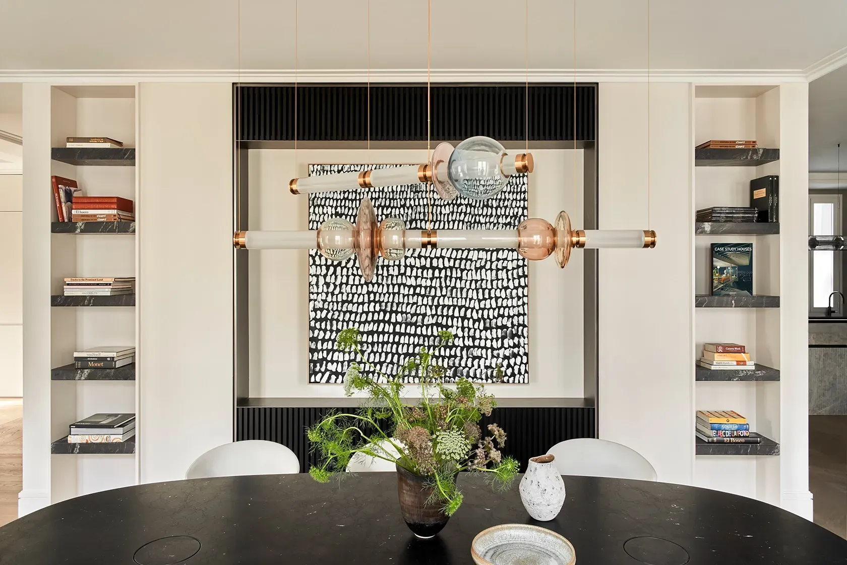 Dining area with black oval table, sculptural chandelier, built-in shelving, and bold monochrome art, creating a refined yet expressive design atmosphere.