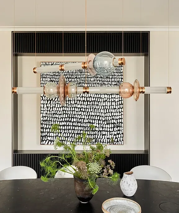Dining area with black oval table, sculptural chandelier, built-in shelving, and bold monochrome art, creating a refined yet expressive design atmosphere.