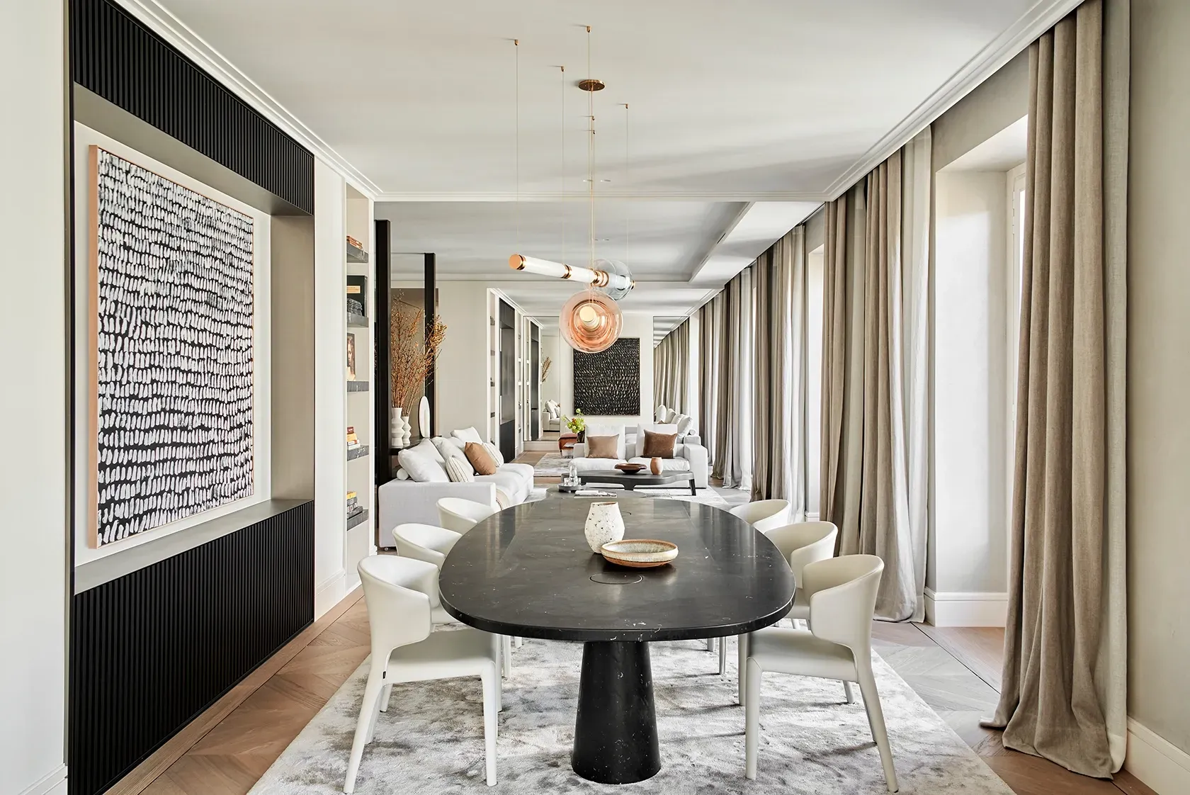 Open-plan dining and living room with statement chandelier, large windows, elegant curtains, and sophisticated art pieces in a luminous, serene interior.