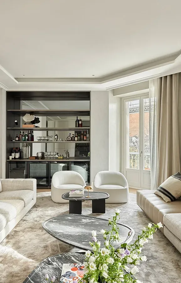 Luxury living room with light neutral sofas, custom bar, modern artwork, and large windows filling the space with warm, natural daylight.