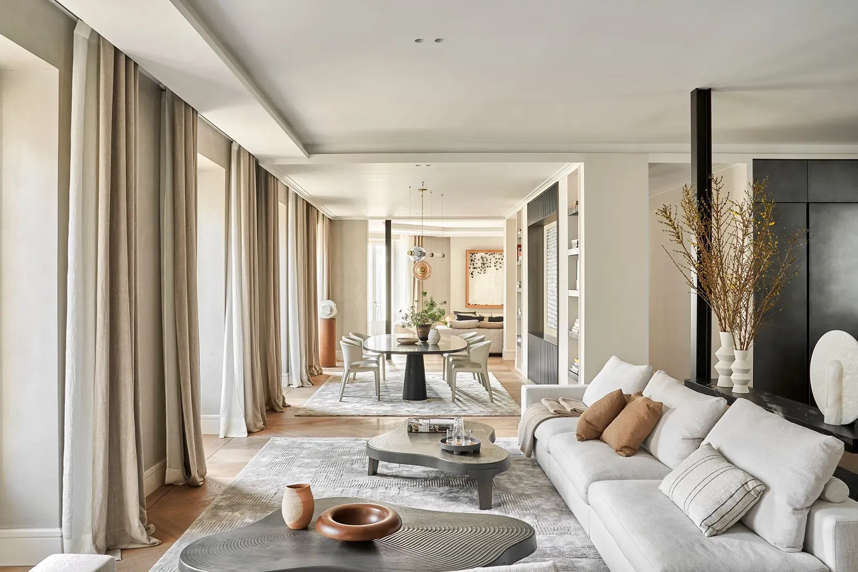 Living area with pale sofas, sculptural decor, and a view towards the dining space, framed by elegant drapes and soft ambient light throughout.
