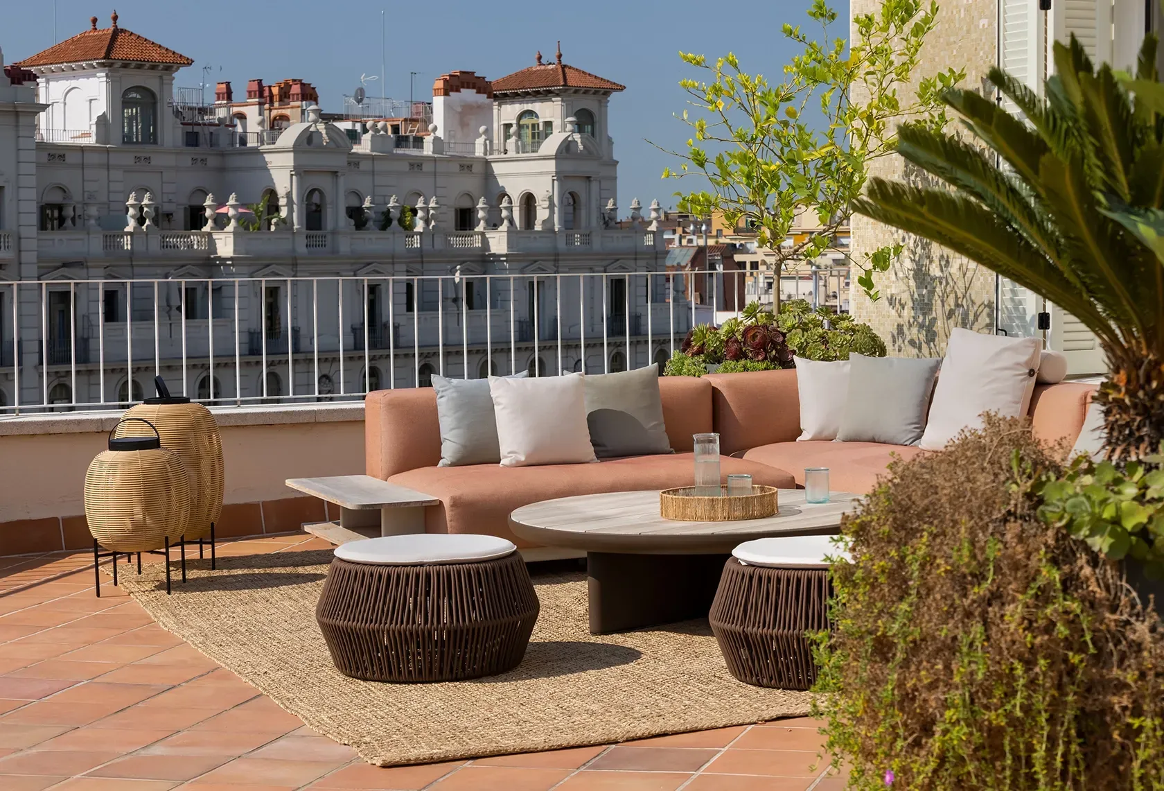 Rooftop terrace with terracotta tiles, peach sofa, woven tables, and city views, combining Mediterranean charm with luxury outdoor living.