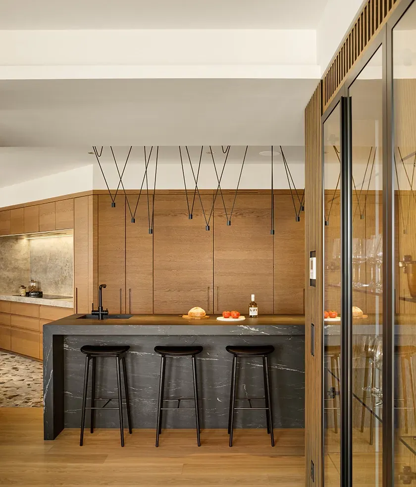 Black marble kitchen island with three stools, pendant lighting, and wood cabinetry, designed by LUV Studio for a refined and modern space.