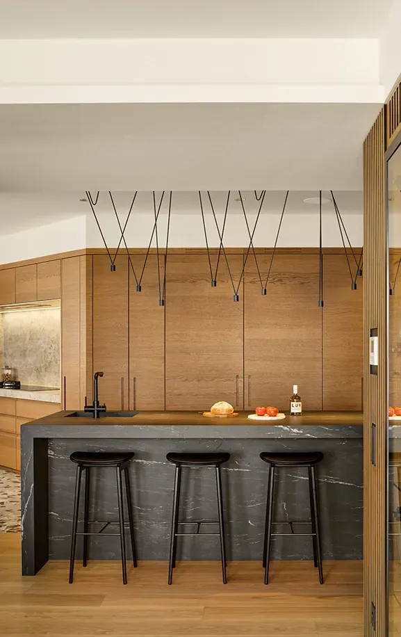 Black marble kitchen island with three stools, pendant lighting, and wood cabinetry, designed by LUV Studio for a refined and modern space.