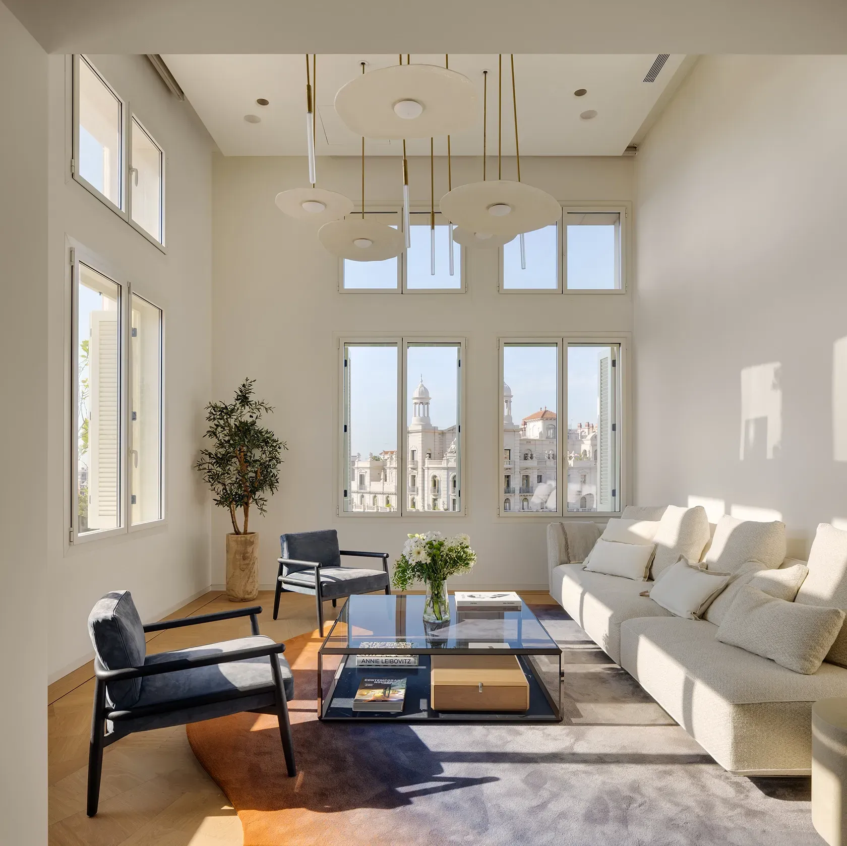 Bright double-height living room with custom pendant lighting, neutral sofas and views over Barcelona’s skyline.