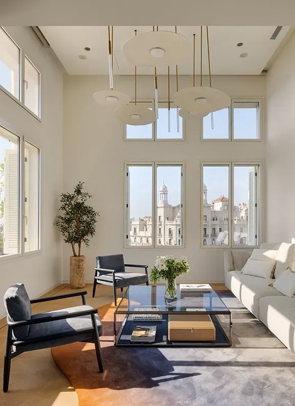 Bright double-height living room with custom pendant lighting, neutral sofas and views over Barcelona’s skyline.