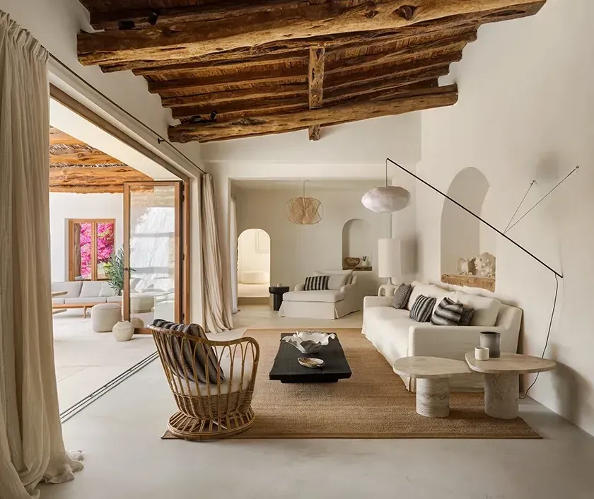 Open-plan living area with exposed wooden beams, neutral furnishings, and a seamless transition to the outdoor lounge with natural light.