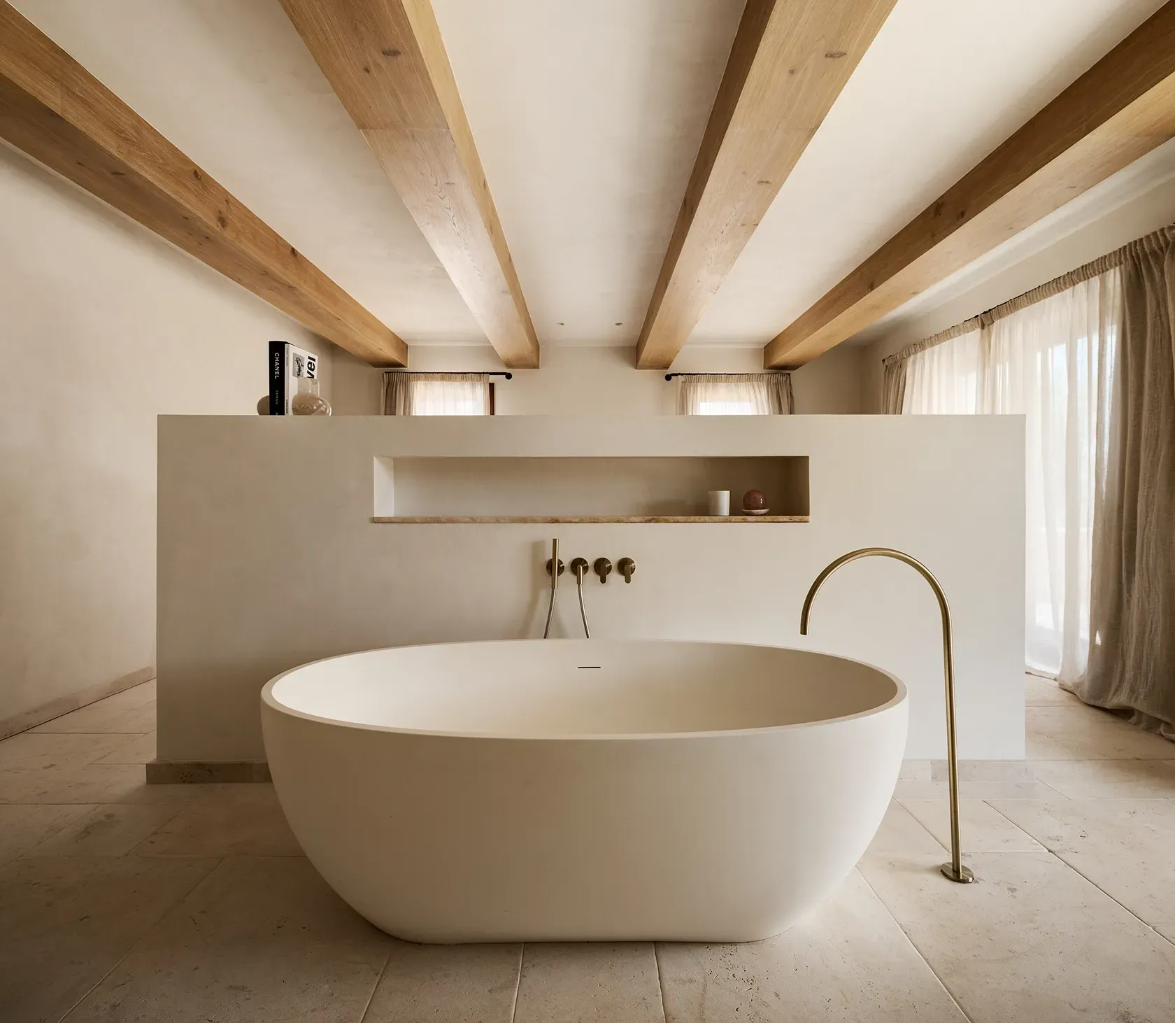 Refined bathroom with sculptural freestanding tub, light wooden ceiling beams, and warm natural light for a tranquil wellness experience.