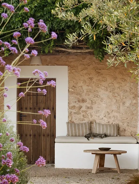 Charming garden nook with stone walls, wooden door, bench seating, and blooming purple flowers—perfect for peaceful moments outdoors.