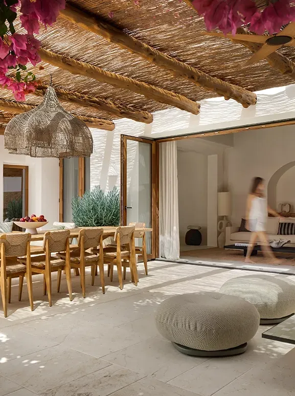 Rustic outdoor dining area with natural wood beams and vibrant bougainvillea, blending luxury and Mediterranean architecture.