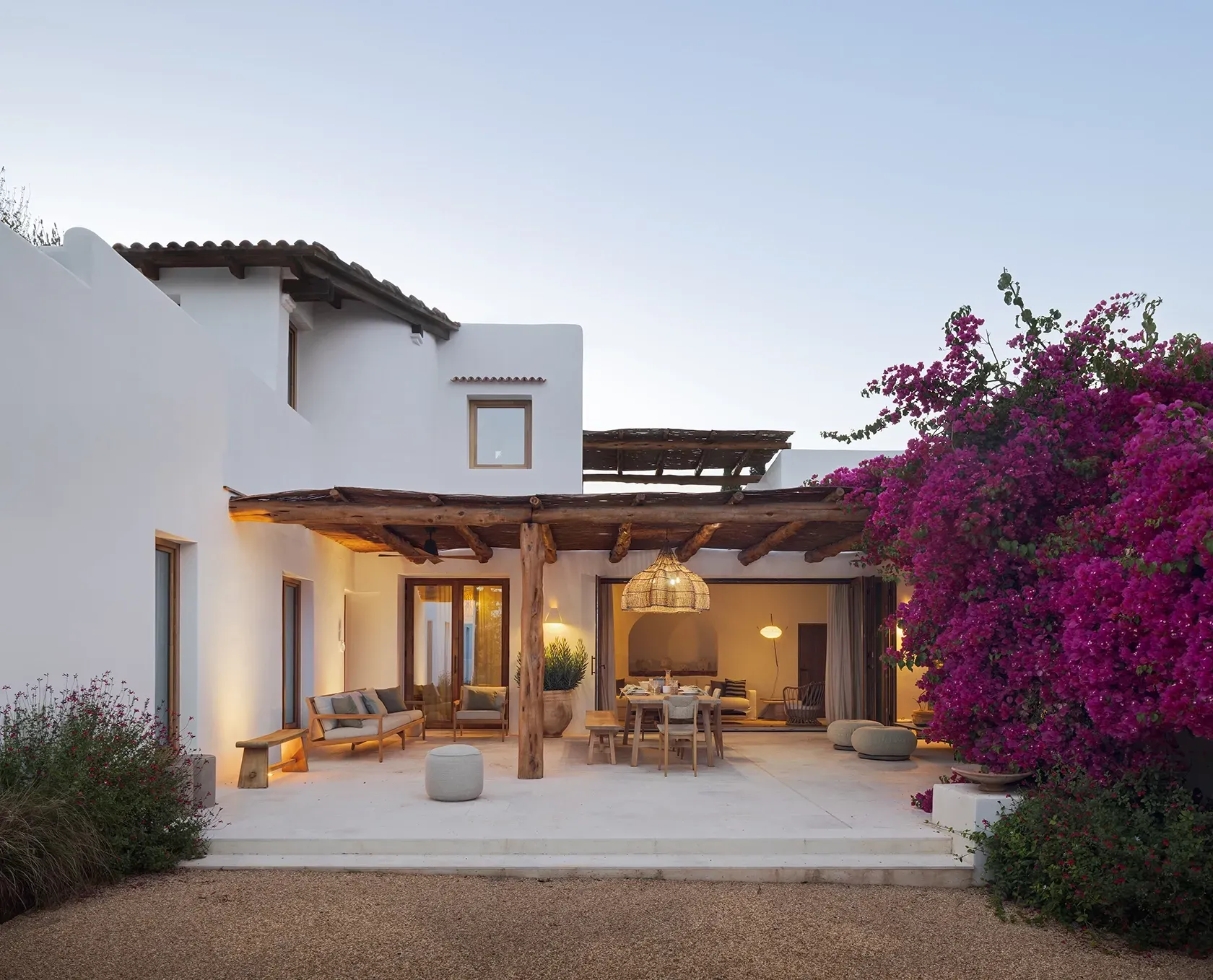 Elegant outdoor dining area under a pergola at night, with soft lighting, natural textures, and blooming bougainvillea enhancing the luxury ambiance.
