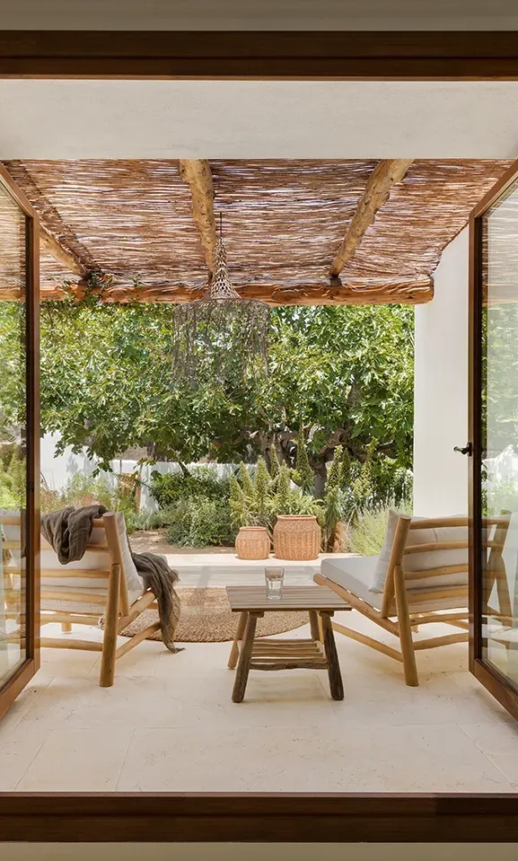 Wood-framed glass doors open to a private terrace with a natural pergola, cozy seating, and lush greenery—blending indoor and outdoor living.