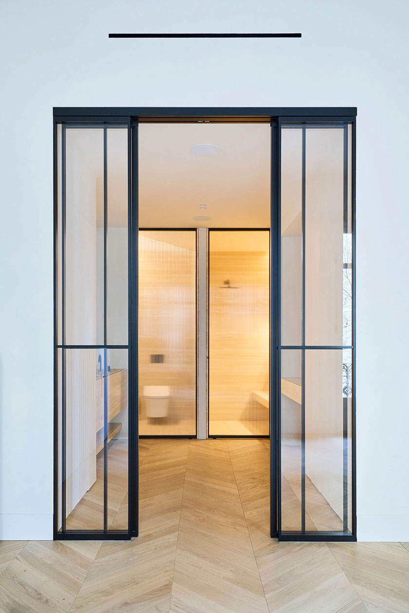 Bathroom entrance framed by black steel and glass doors with warm interior lighting