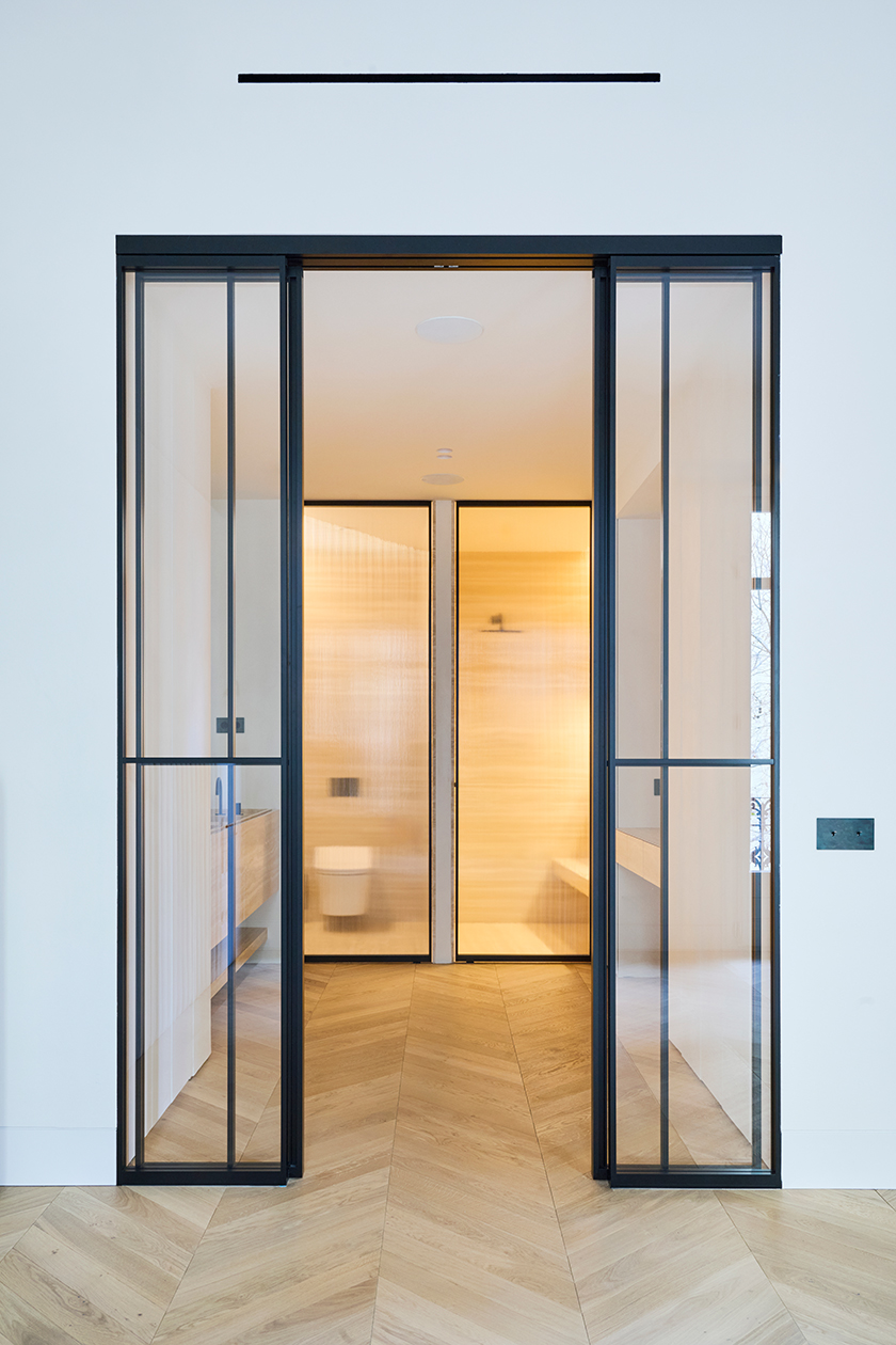 Bathroom access framed by black steel and glass doors with warm interior lighting