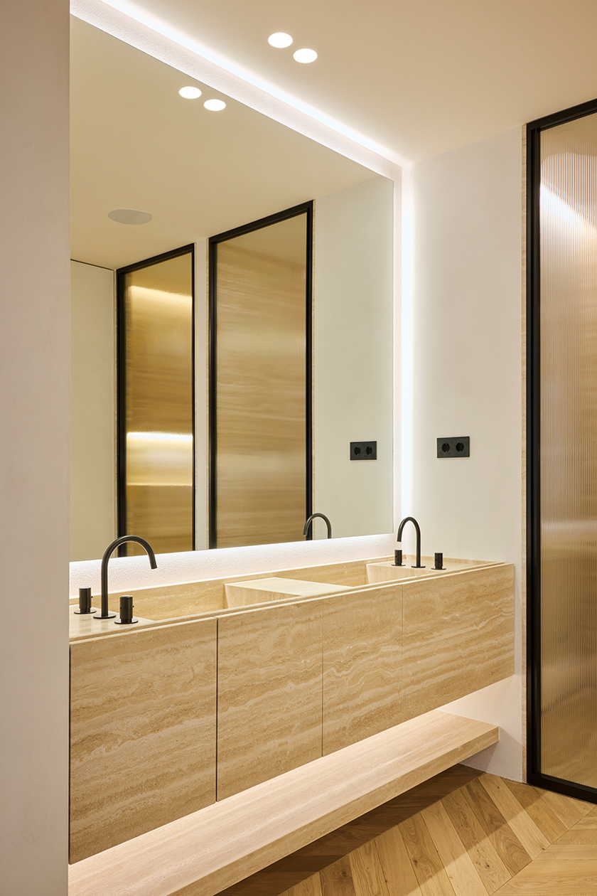 Bathroom vanity in natural stone with integrated sinks, mirror lighting and warm minimalist finishes