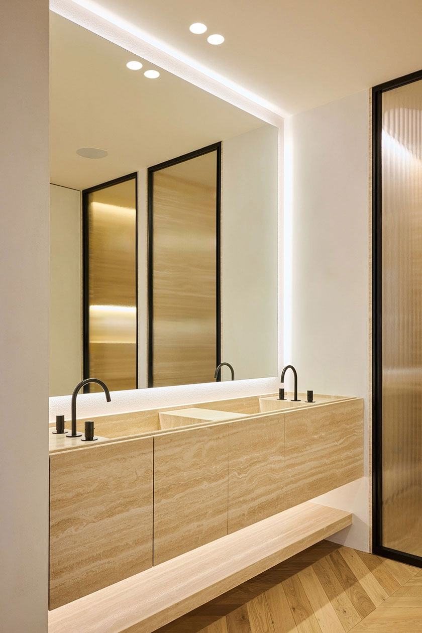 Bathroom vanity in natural stone with integrated sinks, mirror lighting and warm minimalist finishes