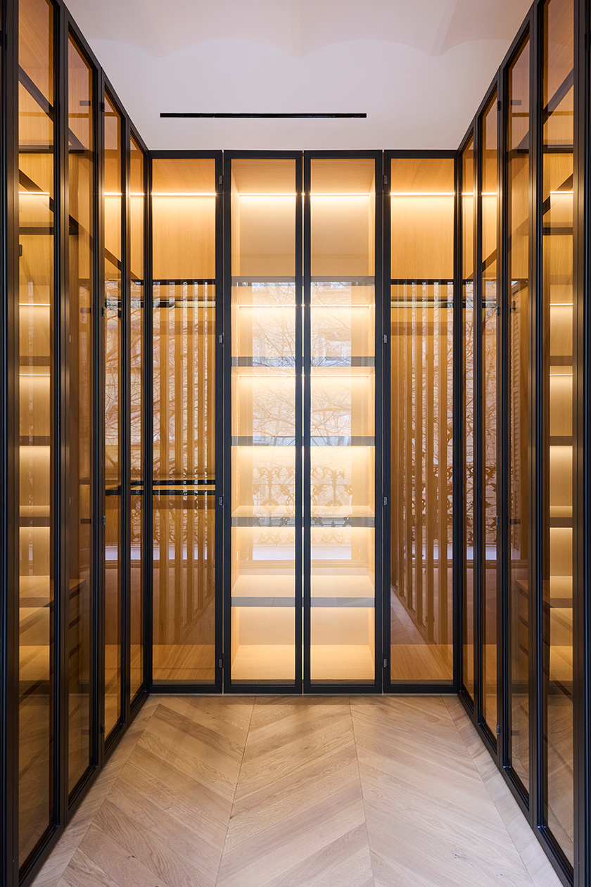 Dressing room with glass wardrobes, integrated lighting and herringbone wood flooring