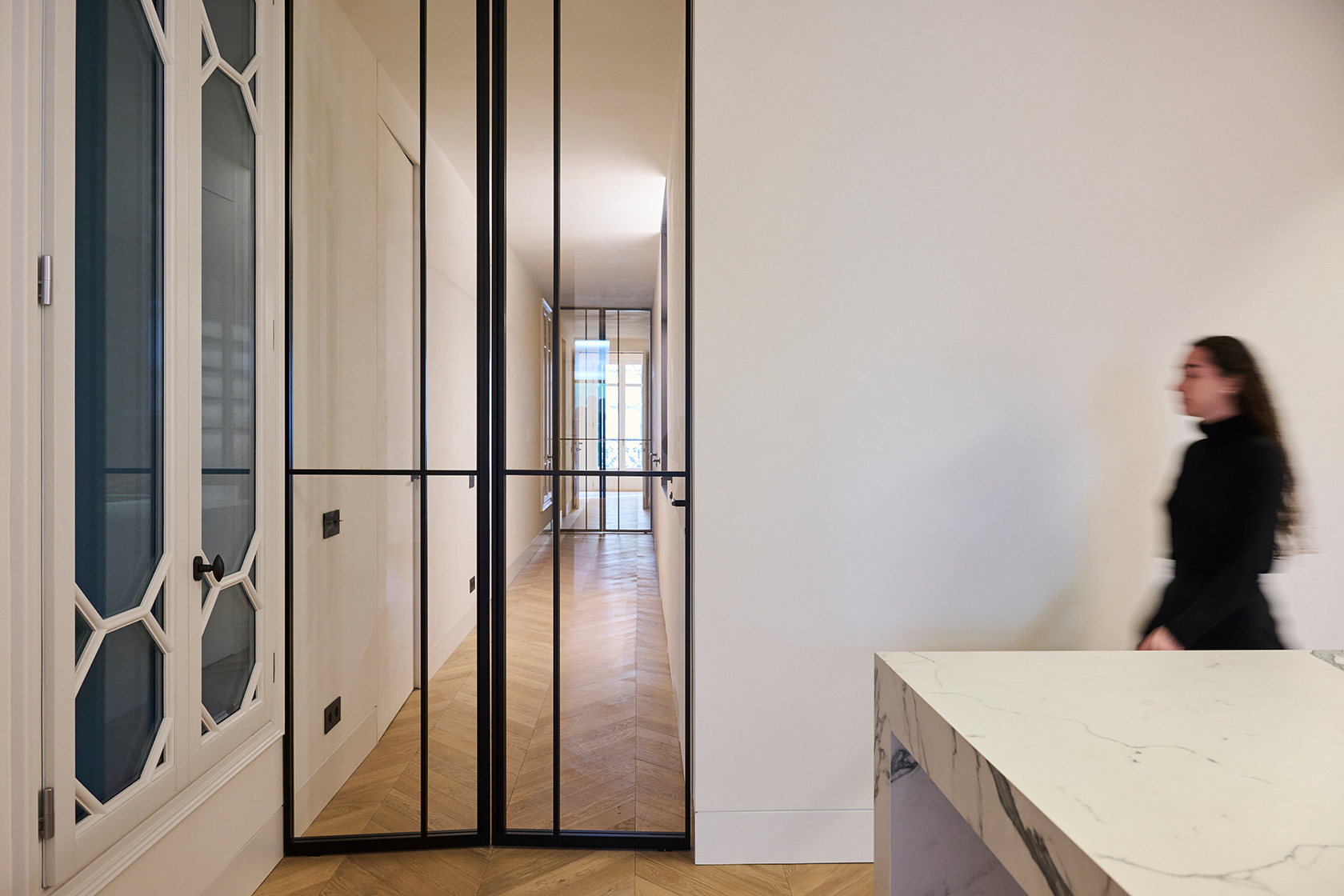 Interior hallway defined by black steel partitions and continuous herringbone wood flooring