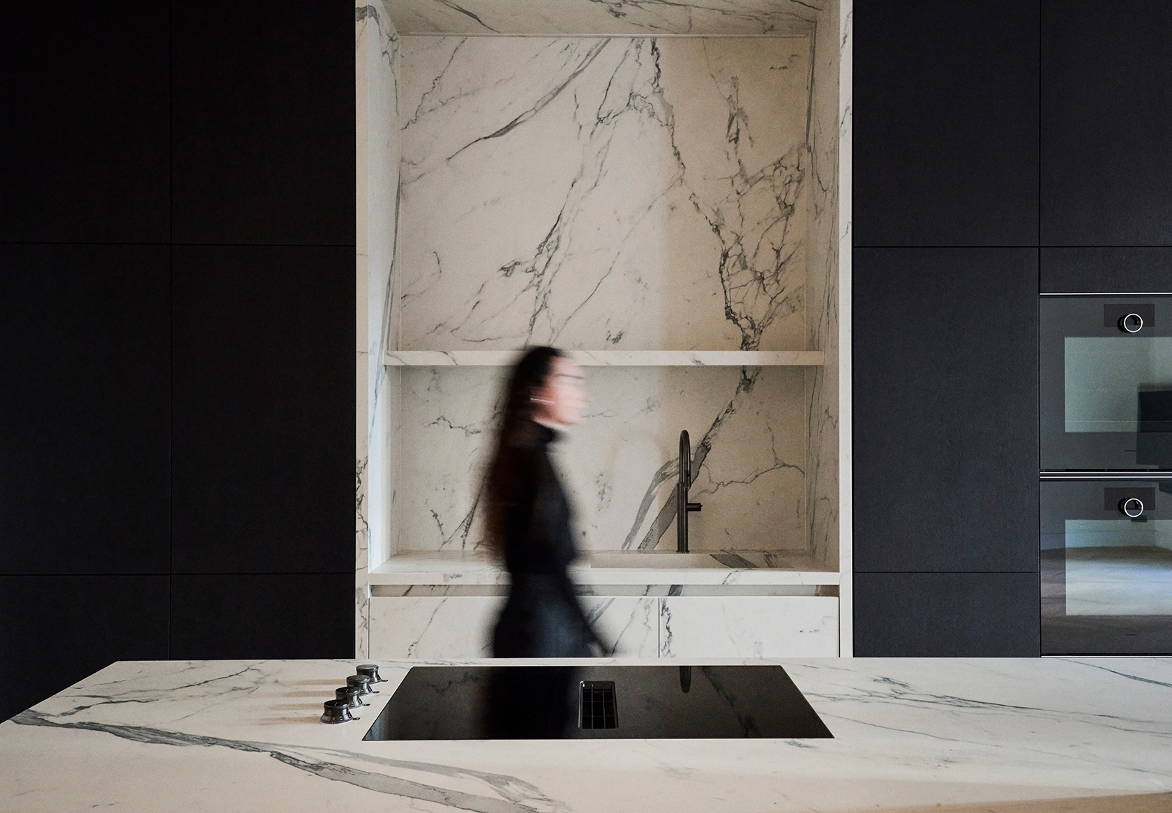 Kitchen island in natural stone with integrated cooktop, contrasted by dark cabinetry and soft lighting