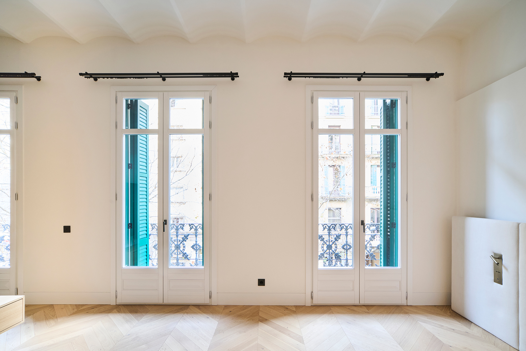 Bedroom with tall windows, green shutters and soft daylight enhancing a calm interior atmosphere