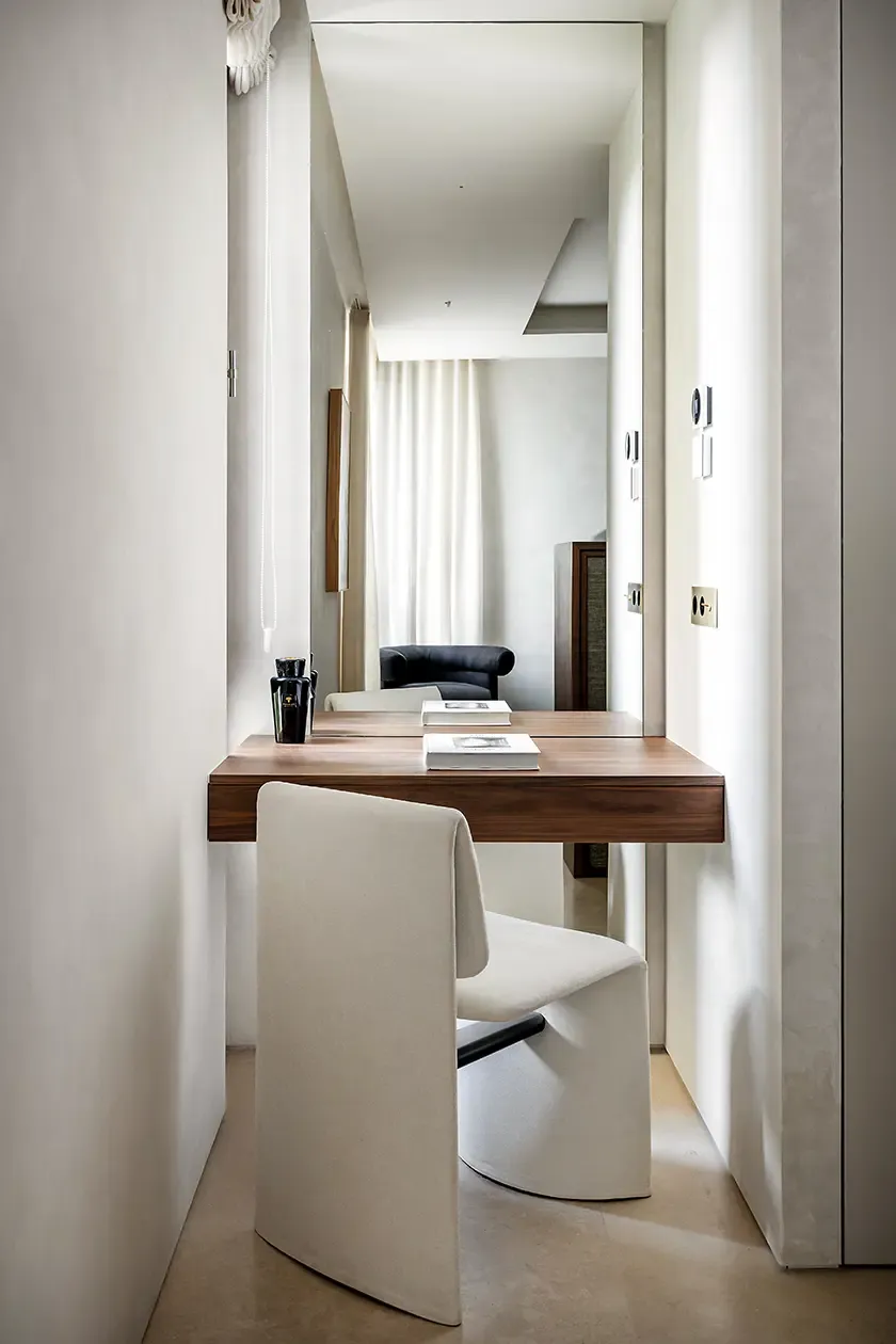 Compact workspace with a floating walnut desk, upholstered chair and full-height mirror, designed as a refined study corner within a contemporary guest bedroom.