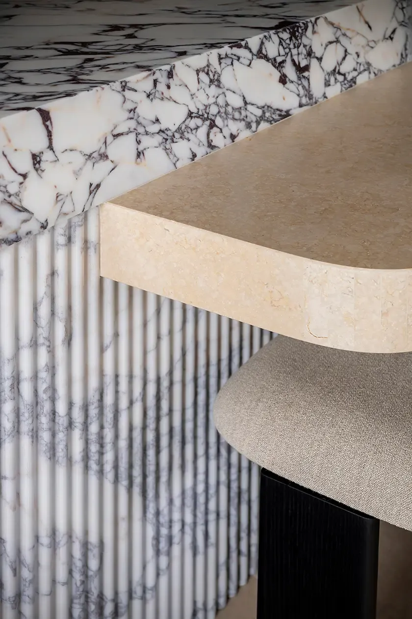 Detail of a bespoke kitchen island featuring fluted marble cladding, a stone countertop and upholstered seating, highlighting material richness and precision craftsmanship.