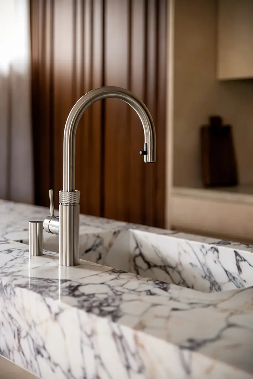 Close-up of a marble kitchen sink with integrated countertop and brushed stainless steel faucet, showcasing premium materials and meticulous detailing in a contemporary kitchen.