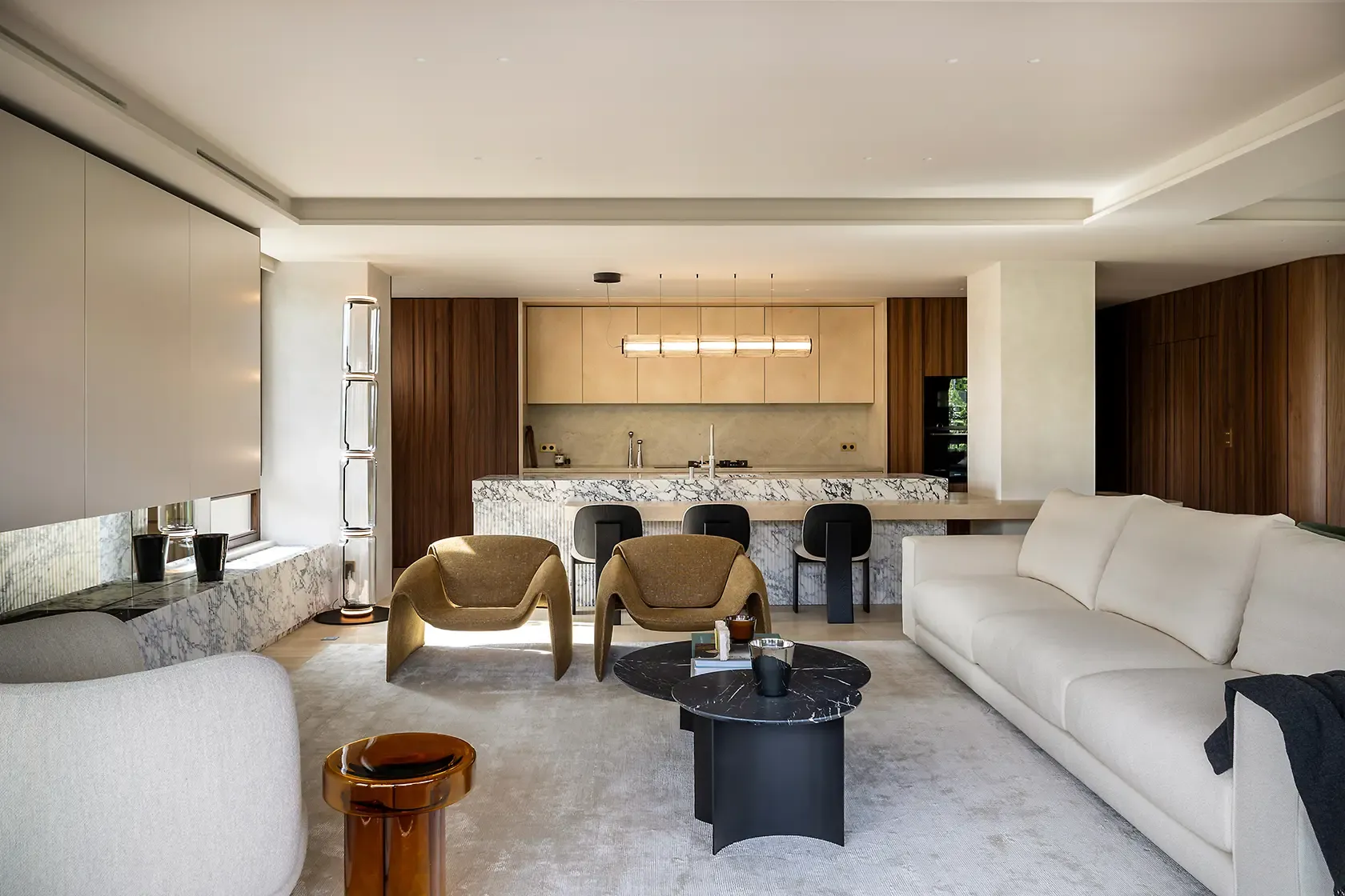 Open-plan living room and kitchen featuring a sculptural white sofa, marble kitchen island, custom walnut cabinetry and curated designer furniture, illuminated by abundant natural light.