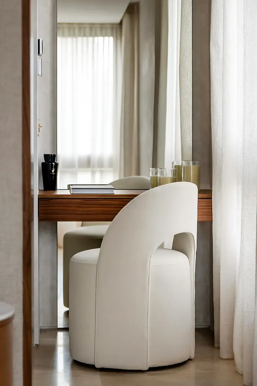Custom dressing table with a walnut vanity, upholstered chair, full-height mirror and soft natural light, reflecting the refined material palette of the master bedroom.