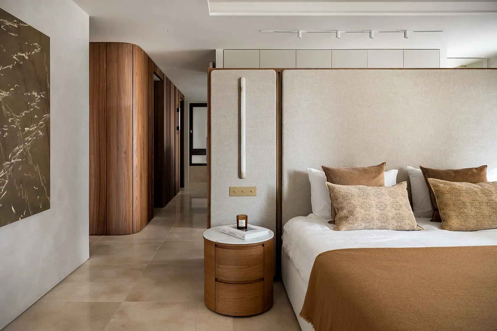 Master bedroom with a custom upholstered headboard, walnut bedside table, soft neutral textiles and curved wood paneling, combining warmth, comfort and contemporary elegance.