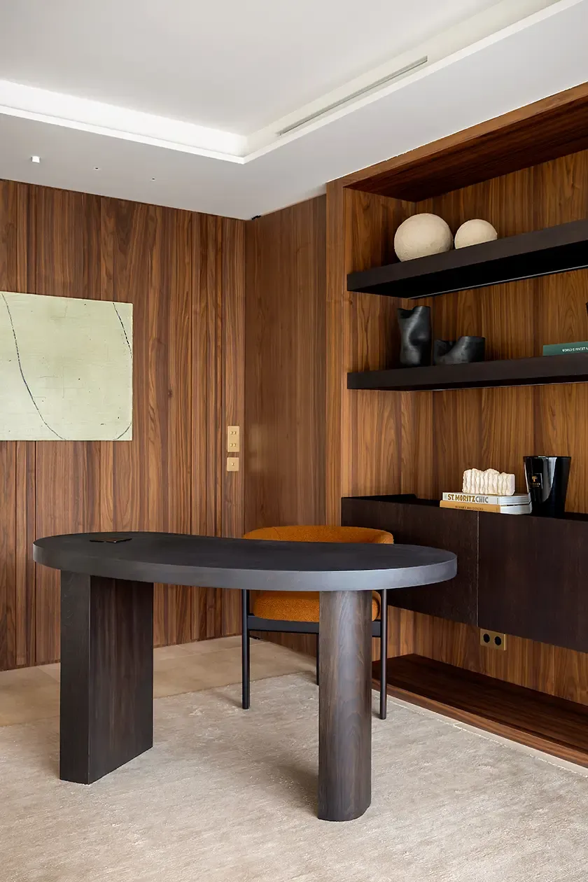 Contemporary home office with a sculptural dark wood desk, custom walnut shelving, textured upholstery and curated decorative objects, creating a warm and sophisticated workspace.