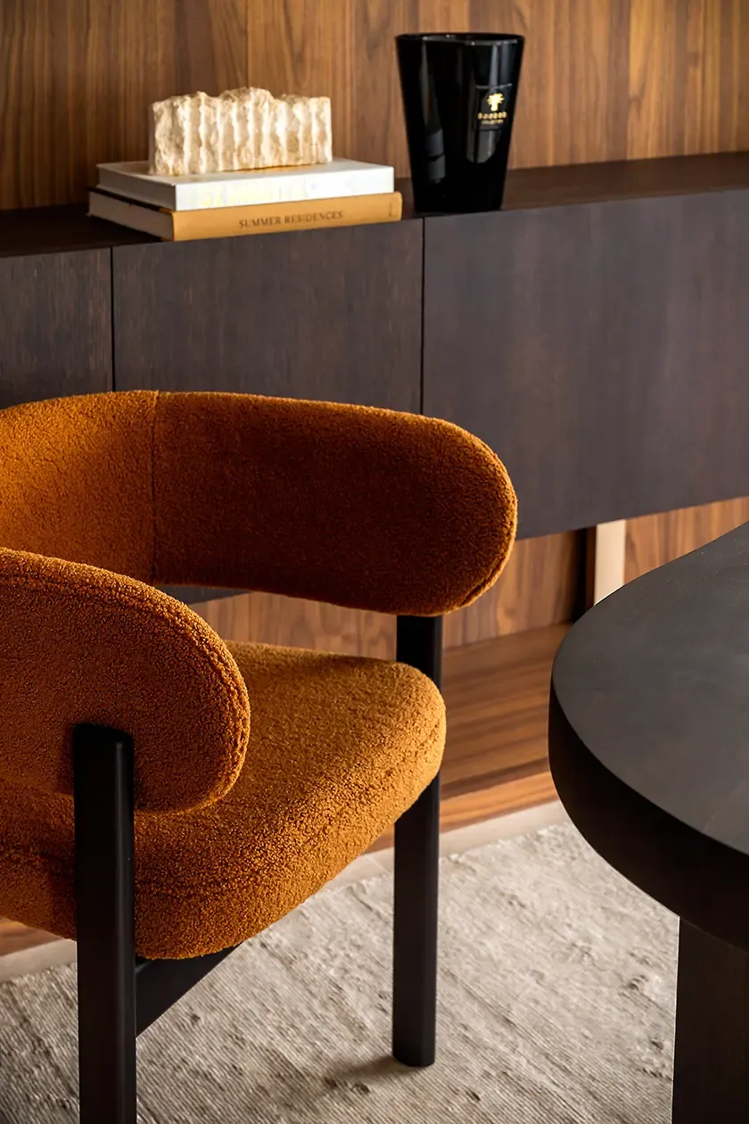 Close-up of an upholstered lounge chair in a home office, paired with dark wood furniture and custom walnut cabinetry, highlighting texture, craftsmanship and contemporary design details.