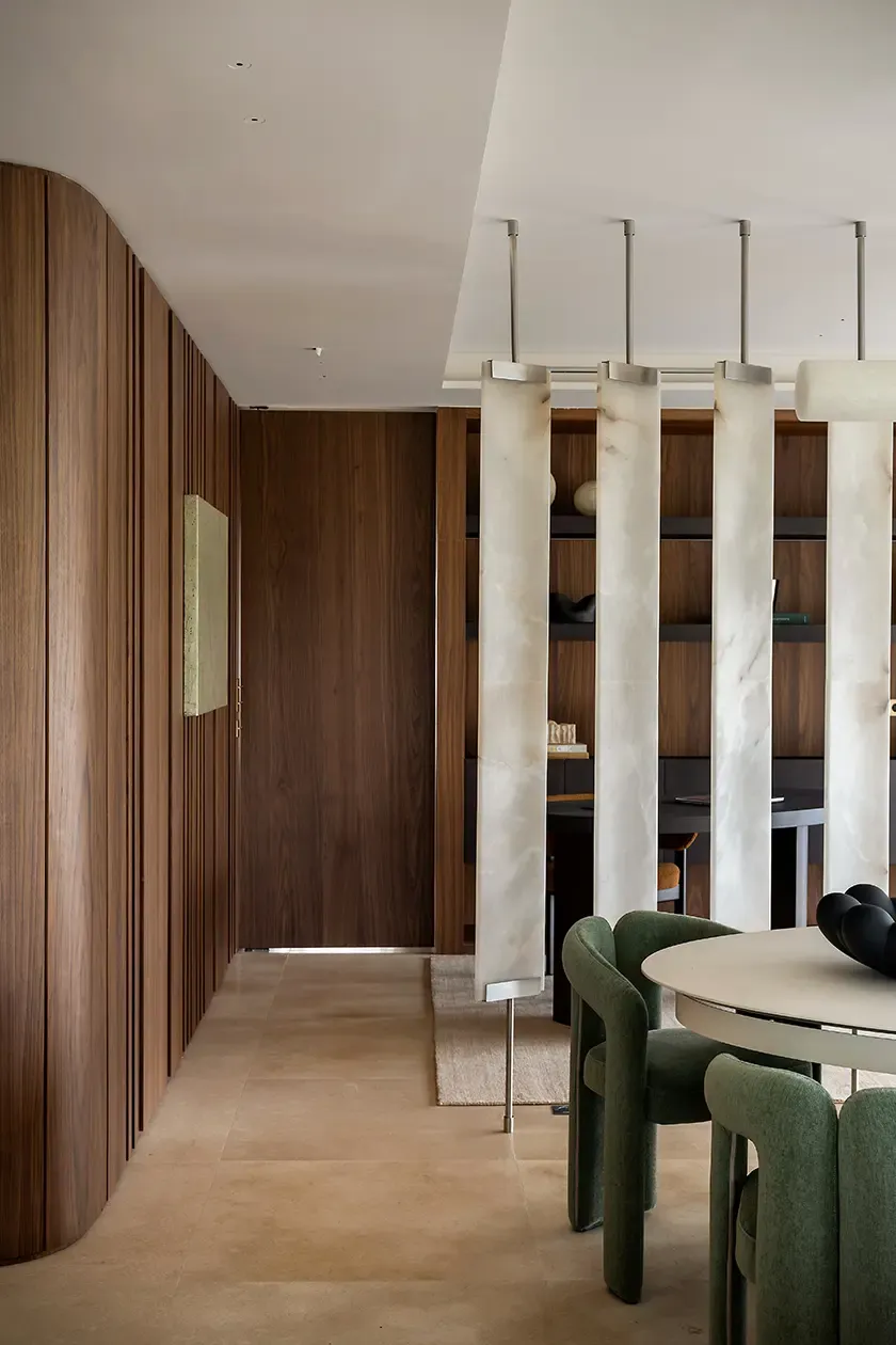 Open-plan interior featuring a sculptural dining area, custom walnut wall paneling, translucent stone partitions and integrated home office, showcasing a sophisticated contemporary layout.