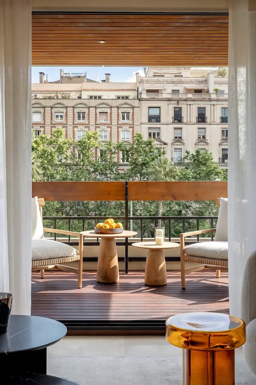 Private terrace with lounge seating, natural wood decking and views over a tree-lined boulevard, extending the living space with abundant daylight and outdoor comfort.