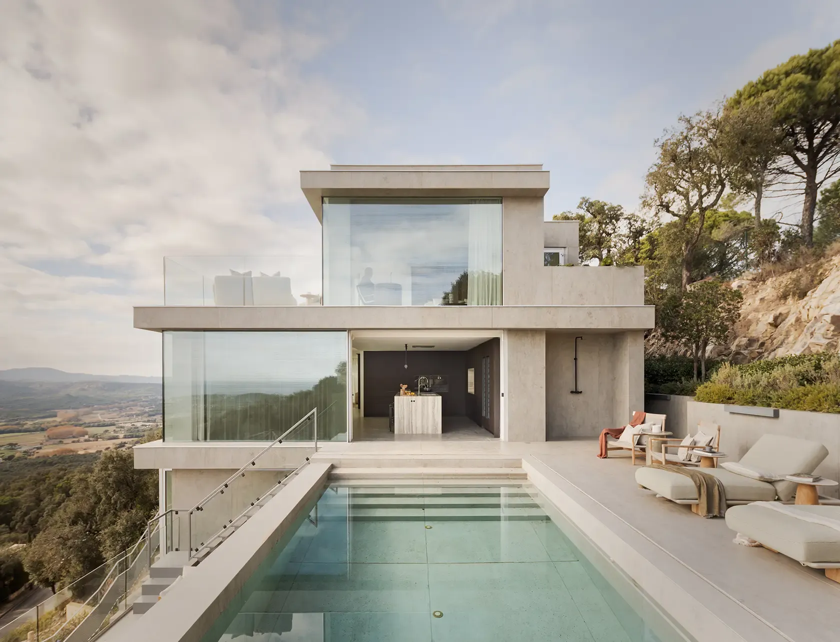 Exterior view of the house, highlighting the sleek modern architecture and large glass windows that frame breathtaking views of the natural surroundings. The minimalist facade blends harmoniously with the landscape.