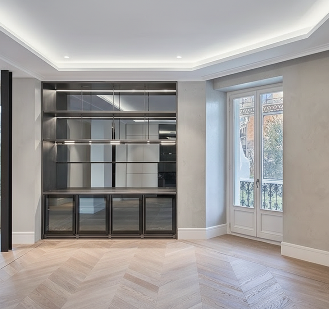 Living area of the Jorge Juan Apartment featuring a bespoke glass-fronted bar corner with metal framing, designed as a refined architectural element that defines the space while preserving visual continuity.