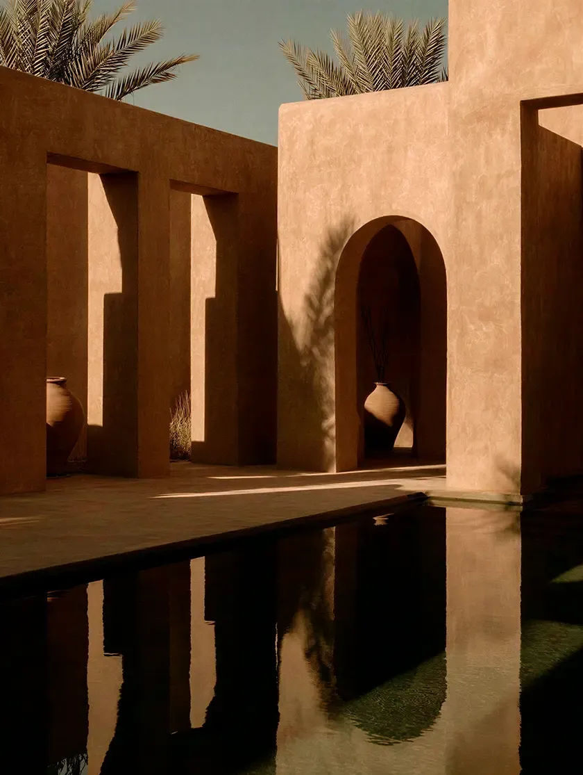 Luxury courtyard with textured earth-toned walls, arched openings, clay vessels and a reflective pool, inspired by contemporary desert architecture.
