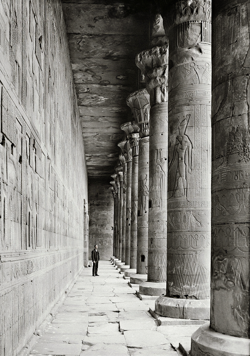 Ancient Egyptian temple corridor lined with monumental carved stone columns and hieroglyphic reliefs, showcasing historic architectural craftsmanship.
