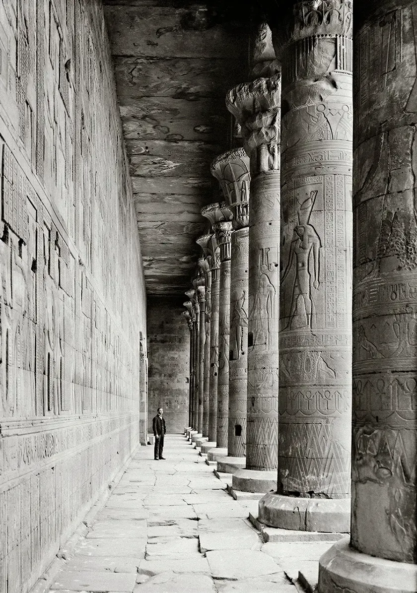 Ancient Egyptian temple corridor lined with monumental carved stone columns and hieroglyphic reliefs, showcasing historic architectural craftsmanship.