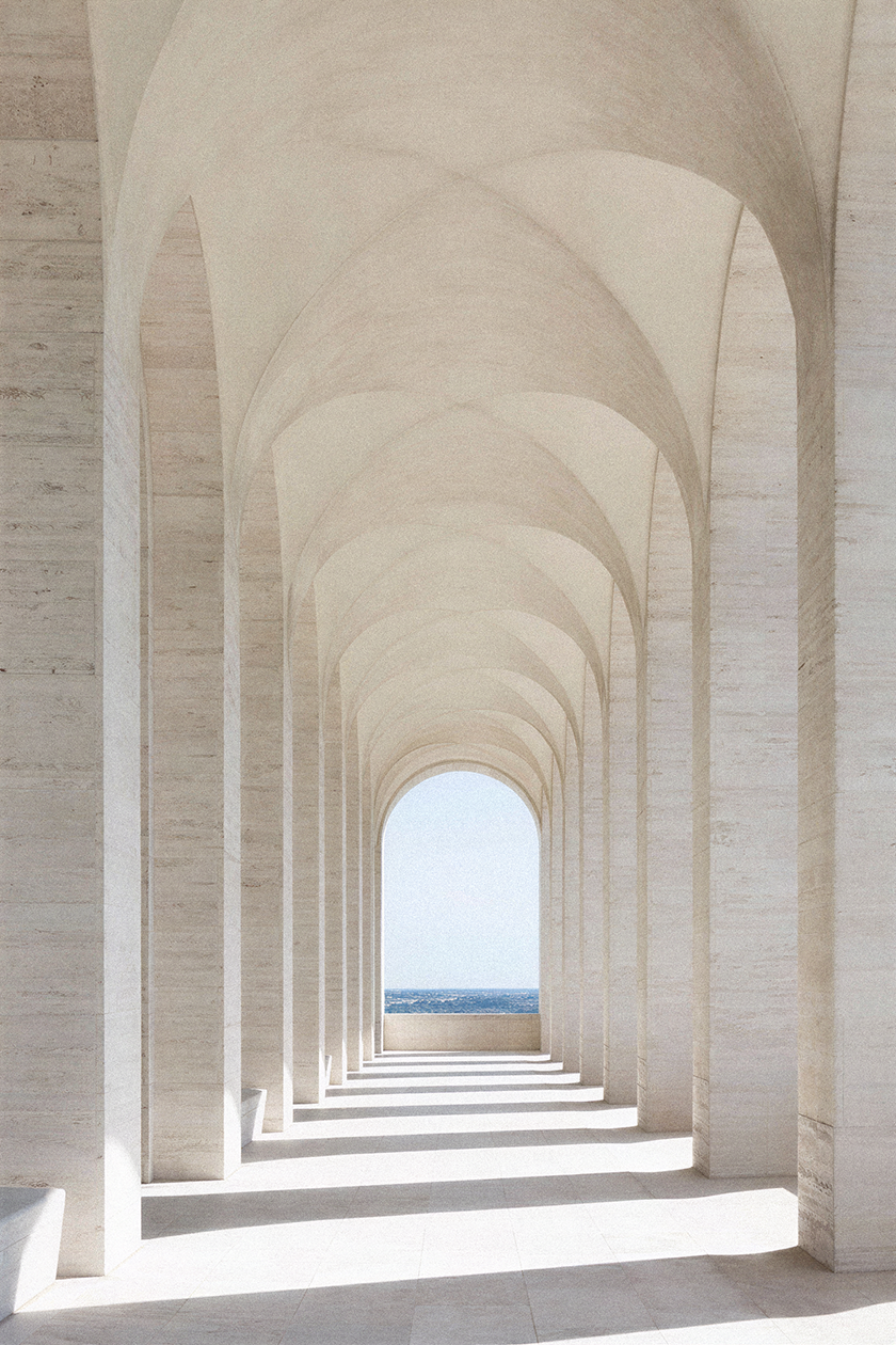 Monumental vaulted colonnade in light stone, featuring rhythmic arches, soft natural light and a framed view of the sea beyond.