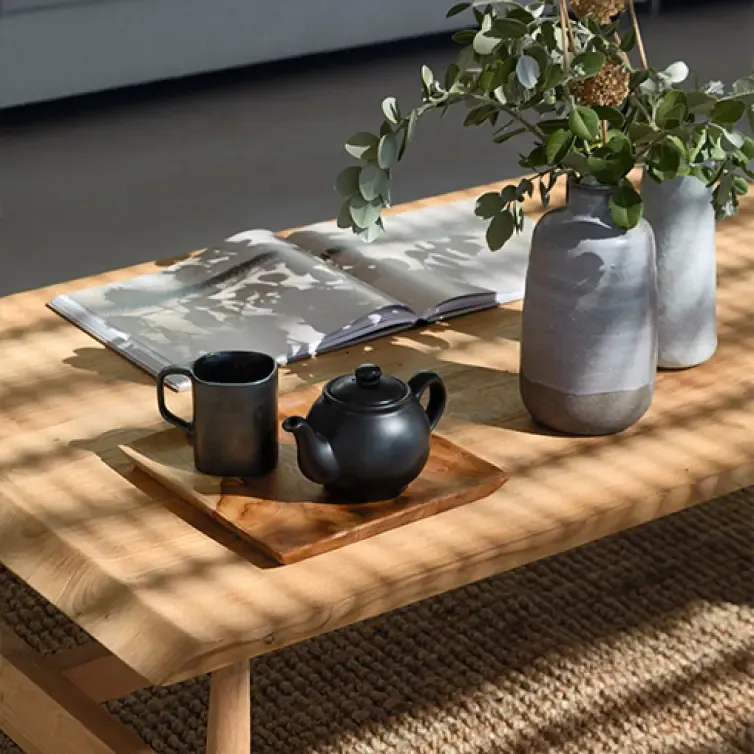 Close-up of a coffee table with ceramic vases, a teapot, and an open book in a cozy interior.