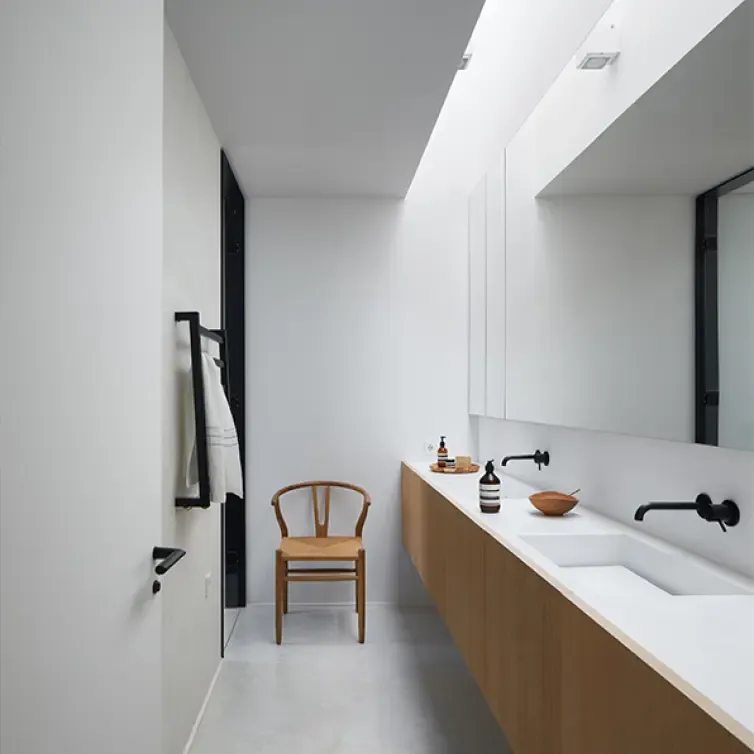 Bright modern bathroom with white walls, wood vanity, and natural light filtering from a skylight.