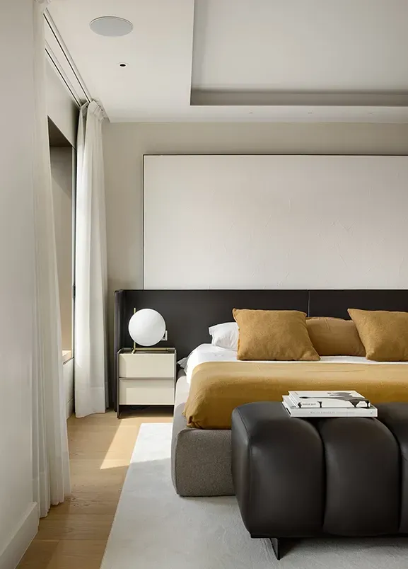 Serene bedroom with natural tones, sleek furnishings, and full-height curtains framing city views.