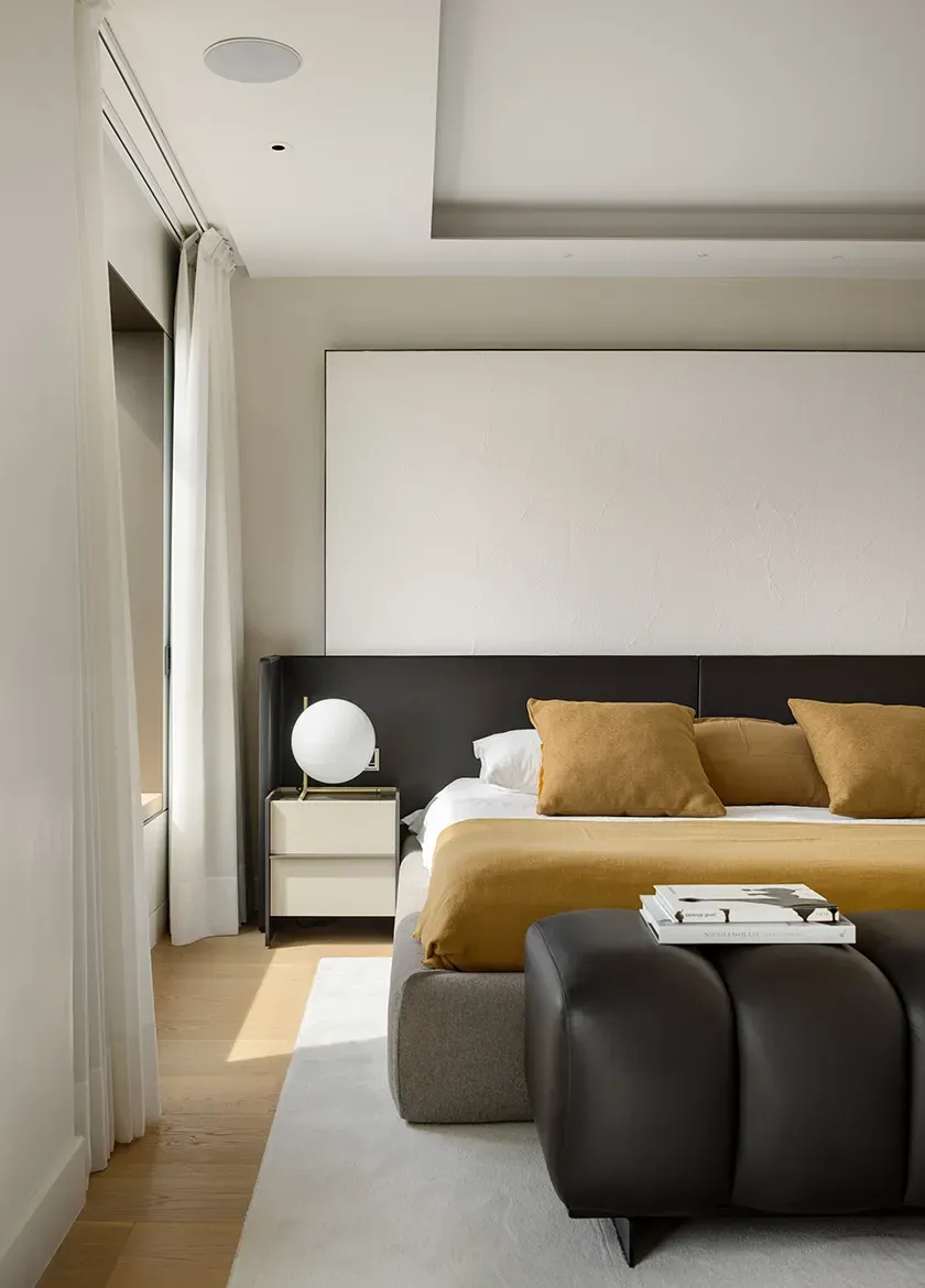 Serene bedroom with natural tones, sleek furnishings, and full-height curtains framing city views.