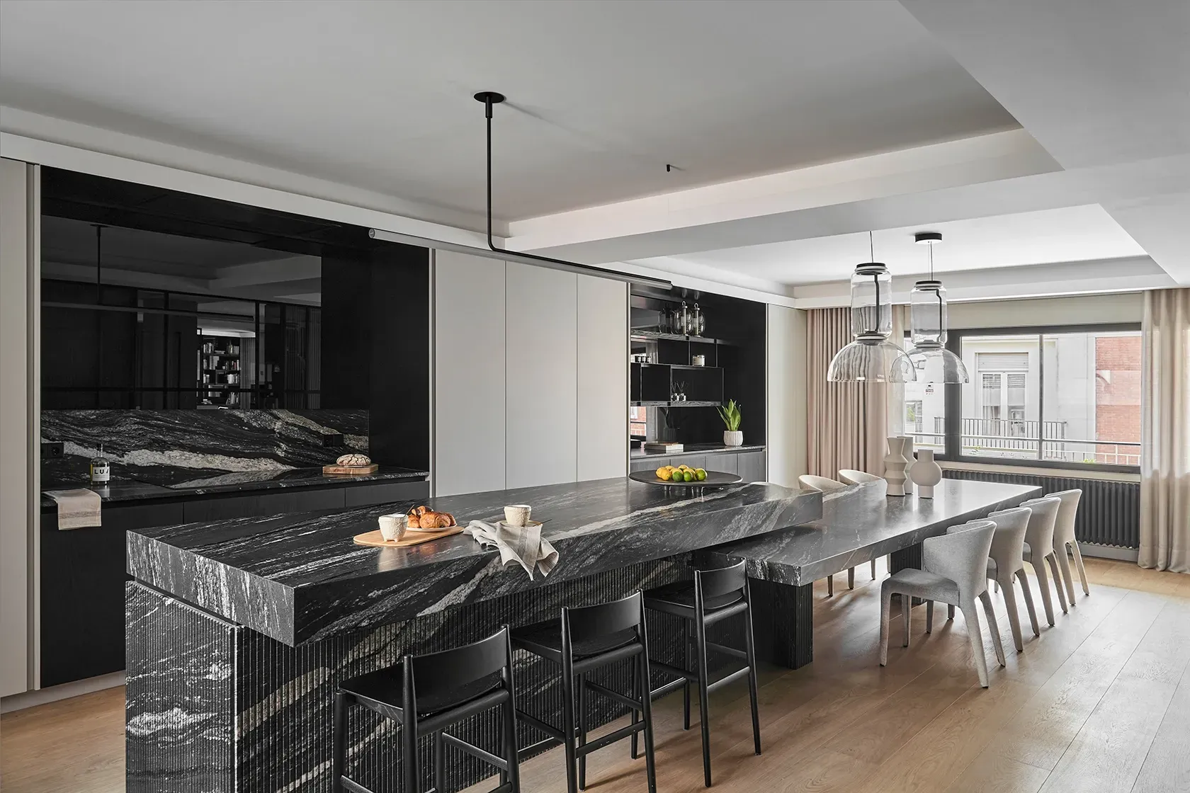 Spacious kitchen with striking stone countertop, long dining table, sculptural lighting, and ample natural light creating a bold, elegant contrast.